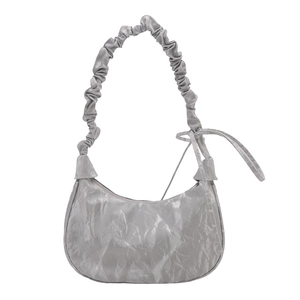 Silver crescent underarm bag with pleated leather texture and bow detail on white backdrop