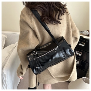 Detail of black glossy cylindrical shoulder bag with silver zipper and adjustable strap