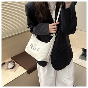 Borsa hobo bianca in pelle lucida esposta su un tavolo con accessori stile di vita