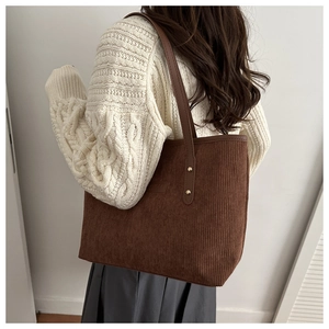 Detail of a dark brown corduroy tote bag worn by a model in a minimalist setting