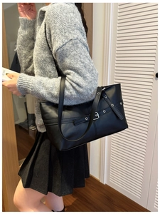 Detail of black PU tote bag featuring silver buckle cross straps and metal eyelet accents