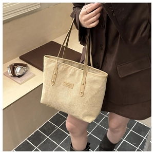 Close-up of beige corduroy tote bag featuring a brand patch and golden rivet details