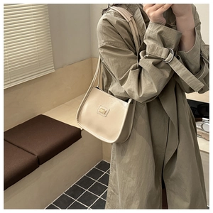 Détail du sac à épaule en cuir blanc crème avec plaque logo dorée sur un trench-coat kaki