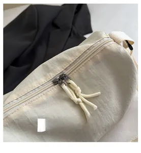 Detail view of smooth double-ended zipper closure with knot pulls on beige nylon bag