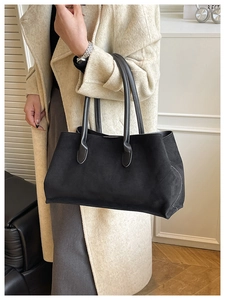 Close-up of black faux suede tote bag with slim leather handles worn with beige coat