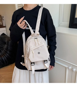 Close-up of a minimalist cream nylon mini backpack with a fashion side label and zip pocket