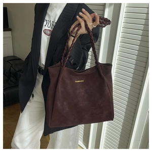 Detail of burgundy faux suede tote bag featuring a thick woven shoulder strap and logo