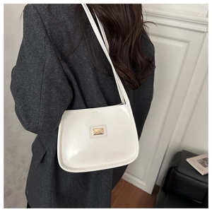 Detail of white glossy leather underarm bag with a gold logo plate on a model's shoulder