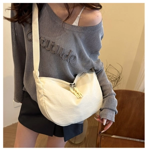 Close-up of stylish off-white oxford cloth crescent bag shown on a model outfit