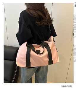 Model wearing a large pink travel bag with black straps in a minimalist indoor setting