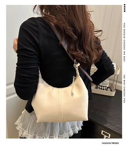 Detail of a creamy white leather hobo bag with vertical stitching and brown shoulder strap