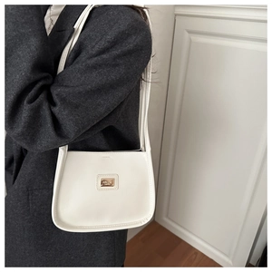 Close-up of a white crescent shoulder bag with a sleek metal logo on a grey blazer