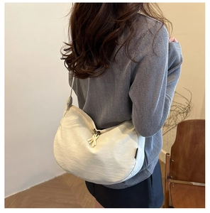 Detail shot of beige crescent crossbody bag showing smooth fabric texture and knot zipper