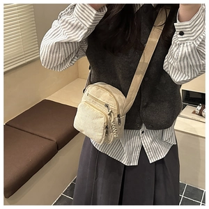 Detail of cream corduroy crossbody bag featuring multi-zipper pockets and striped texture