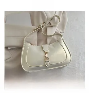 Detail of a creamy white half-moon underarm bag with golden metal buckle and smooth texture