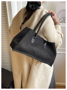 Detail of a large black faux suede tote bag worn with a beige coat for a minimalist look