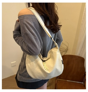 Detail of white canvas half-moon bag featuring wide shoulder strap and knot zipper pull