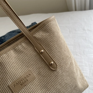 Beige corduroy tote bag with leather label and gold rivets on a soft background