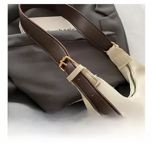 Close-up of contrast leather shoulder strap with golden metal buckle on ivory tote bag