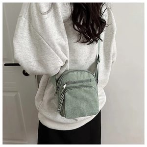 Detail of light green corduroy crossbody bag featuring dual front zipper pockets