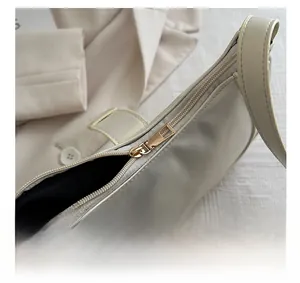Detailed close-up of smooth gold metal zipper and black lining on cream shoulder bag