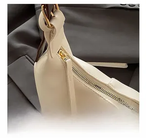 Close-up of golden zipper detail and brown leather strap on cream white shoulder bag