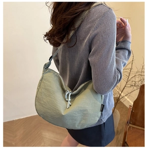 Detail view of sage green crescent nylon shoulder bag with knotted cord and brand tag