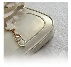 Detail shot of precise stitching and gold hook on a cream leather baguette handbag
