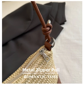 Detail of woven straw handbag featuring silver zipper hardware and brown leather strap