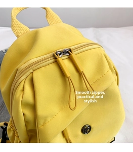 Detailed close-up of smooth double zippers and round metal buckle on a yellow nylon backpack