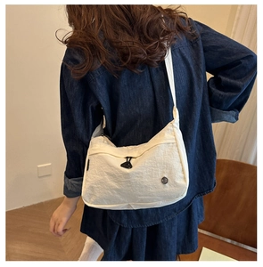 Detailed side view of a cream nylon crescent shoulder bag on a model showing drape
