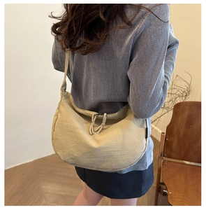 Detail of beige pleated crescent bag with adjustable drawstring closure worn by model