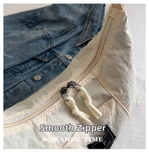 Macro shot of smooth metal double zippers and fabric tag on beige nylon crossbody bag