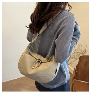 Detail of beige crescent bag featuring textured fabric and decorative knot zippers