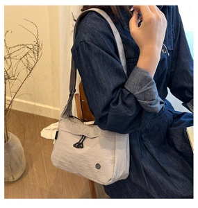 Gros plan du sac bandoulière en nylon gris clair avec sangle et logo détaillé