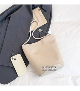 Beige pebble leather bucket bag shown next to a smartphone for scale comparison