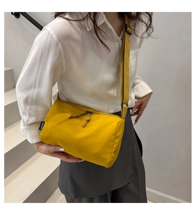 Detail of a bright yellow nylon crossbody bag featuring woven texture and zipper tassels