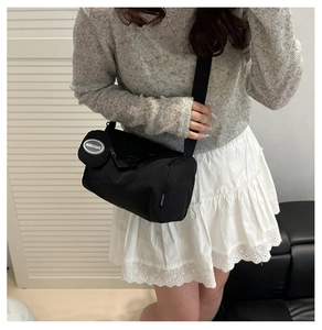 Detail of a black cylindrical crossbody bag with a round charm on wide nylon shoulder strap