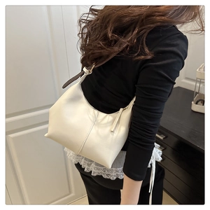 Detail of a creamy white tote bag with vertical stitching and brown shoulder strap