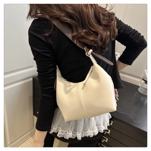 Detail of cream crescent shoulder bag with brown strap worn by model in minimalist setting