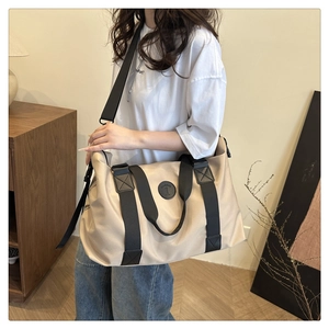 Close-up of beige travel duffel bag with black straps and fashion logo patch