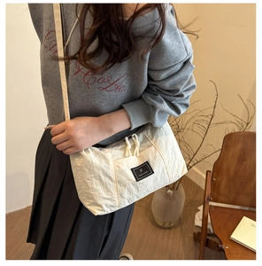 Detail of white wrinkled nylon crossbody bag featuring black logo patch and rope zipper pull