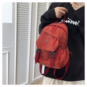 Detail of brick red nylon mini backpack showing front flap and dual buckle straps