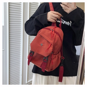 Detail of red water-resistant nylon backpack featuring adjustable black buckles and drawstrings