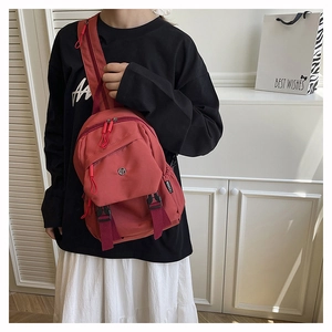 Detail view of red nylon chest bag featuring front zipper pockets and circular metal logo
