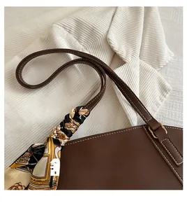 Detail of a brown leather tote bag with white stitching and a vintage floral silk scarf
