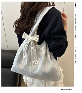 Detail of blue organza tote bag featuring white floral embroidery and a lace bow