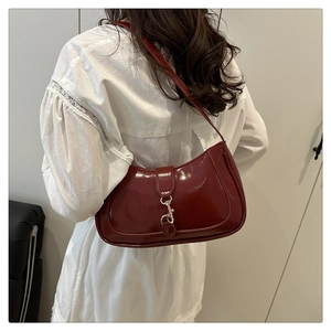 Detail einer burgunderroten Lackleder-Hobo-Tasche mit Silberschnalle an einem Model