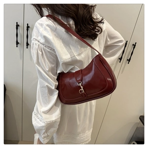 On-shoulder view of a glossy wine red crescent underarm bag with gold metal clasp