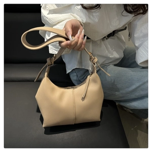 Close-up of minimalist beige leather underarm bag with sleek stitching on dark sofa
